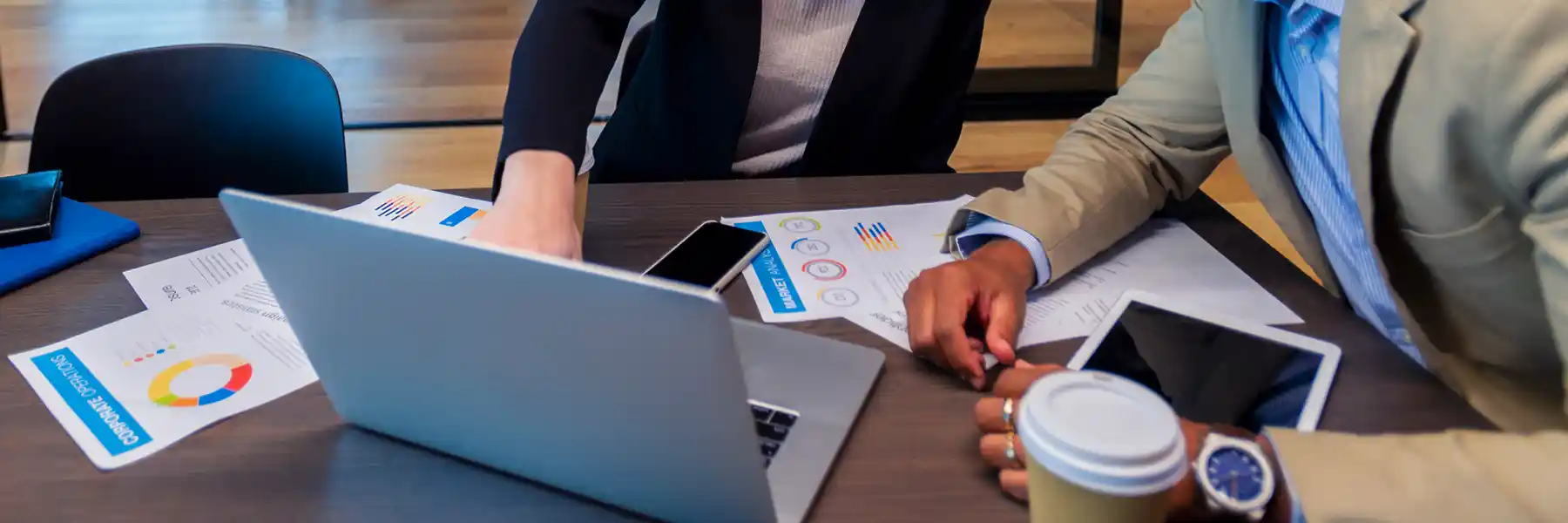 Two people work at a table with a laptop and papers